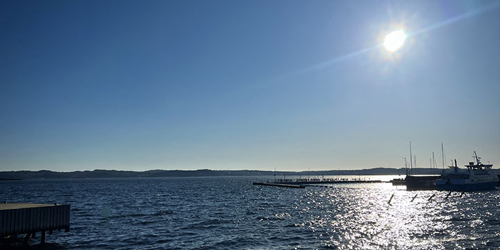 en blåtoning bild på havet, solen skiner på himlen och i bakgrunden skymtas några båtar i hamnen